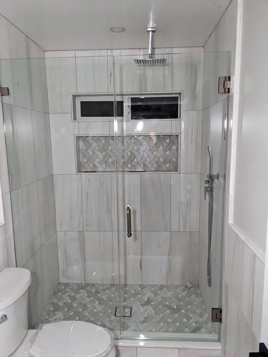 Frameless glass shower door in a tiled walk-in shower with a mosaic niche