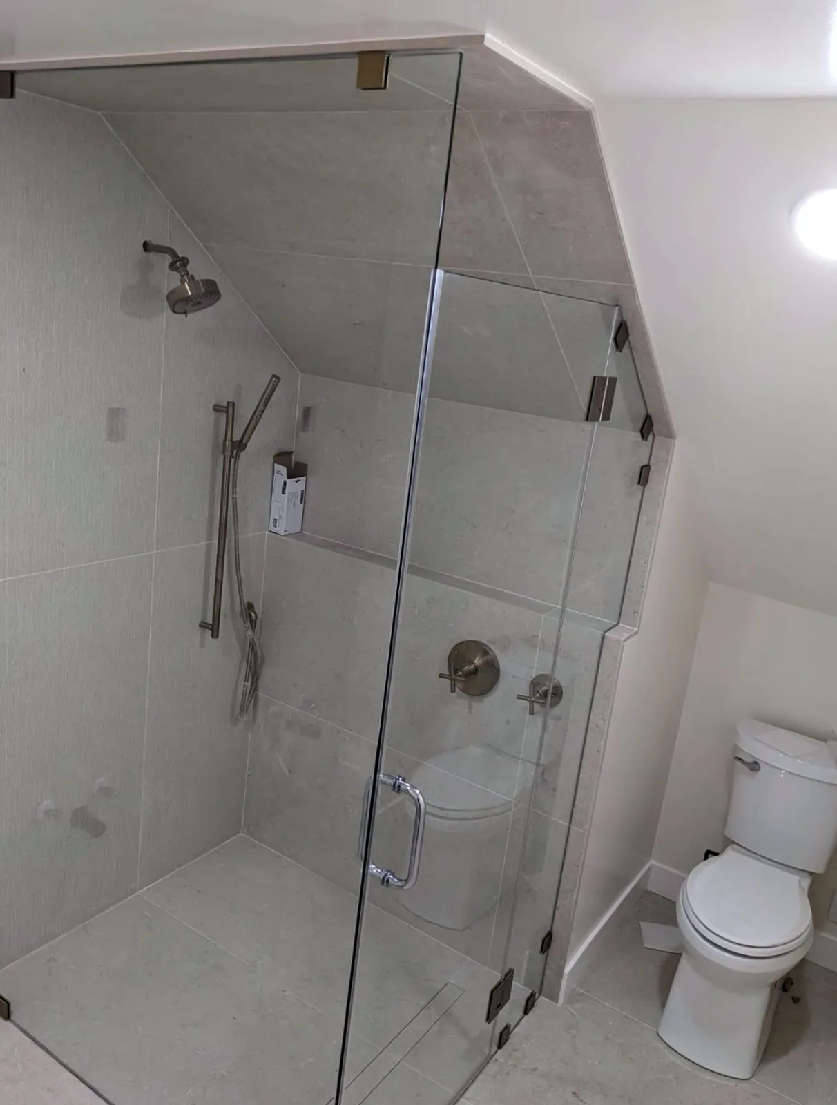 Custom frameless glass shower enclosure cut to fit under a sloped ceiling