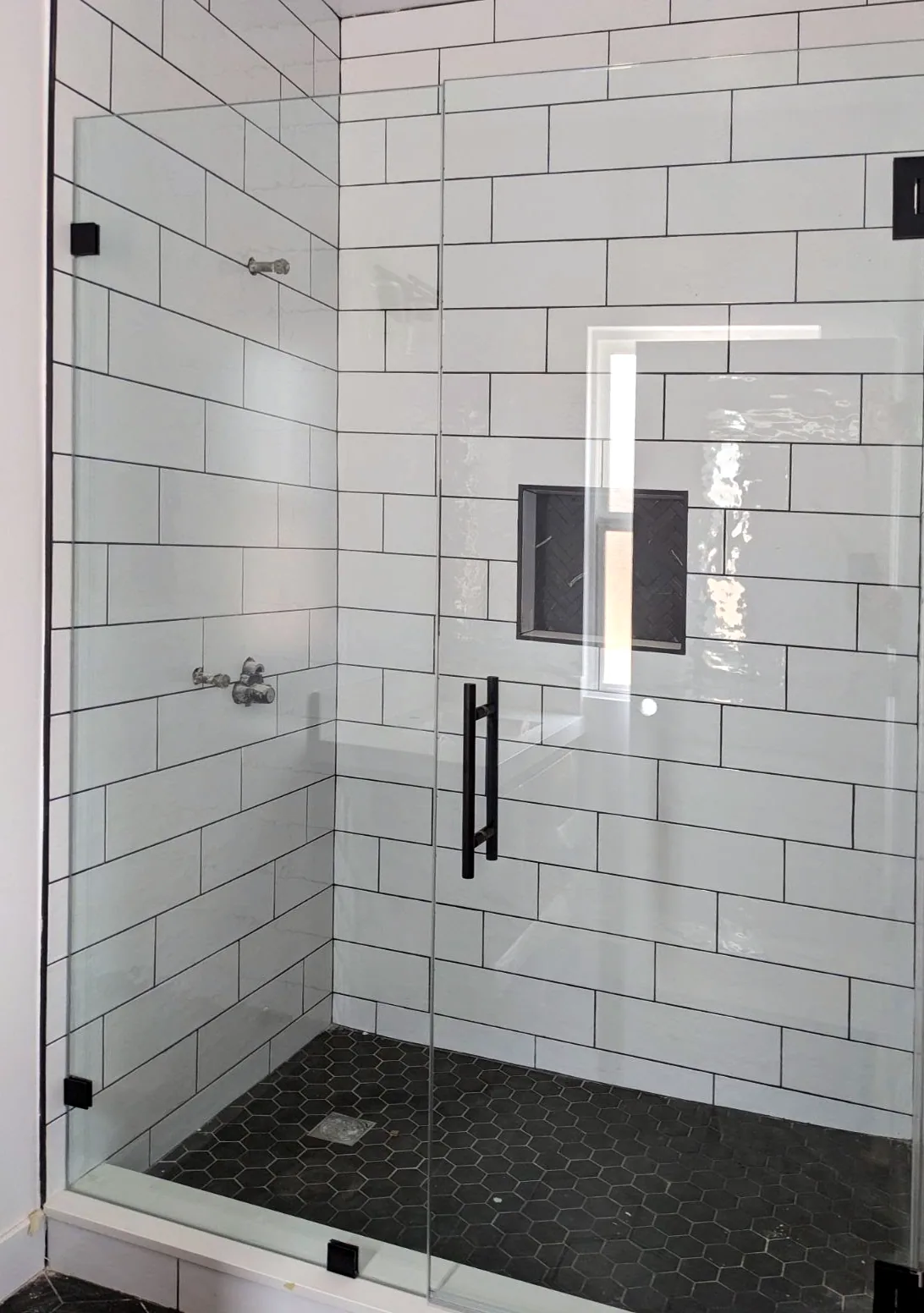 Frameless glass shower in white subway tile with a matte black handle